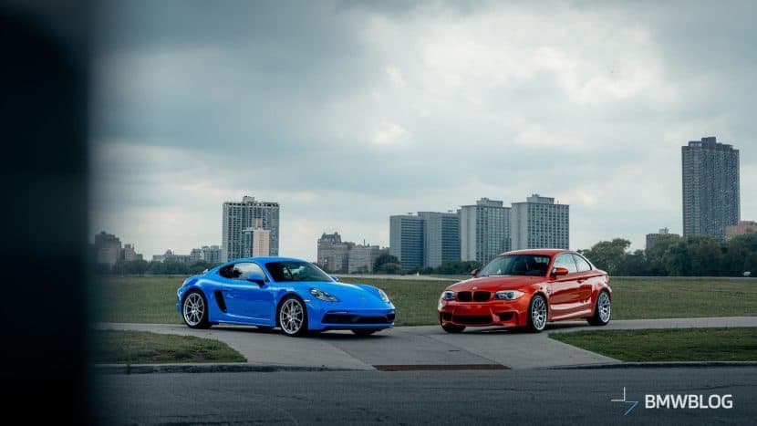BMW 1M Coupe in Valencia Orange and Porsche 718 Cayman GTS 4.0 in Shark Blue parked side by side, highlighting their distinct design and color contrast.